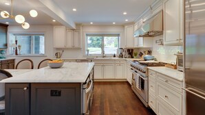 A modern kitchen with white cabinetry, a marble island, stainless steel appliances, and a large window providing natural light. - Outdoor Entertainment Areas: Spacious Katonah Gem! (Katonah)