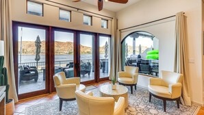 A spacious room with a large sliding glass door leading to a patio area with outdoor furniture. There is a ceiling fan, a round coffee table, and several chairs. - Game Room + Dock: Riverfront Escape in Parker! (Parker)