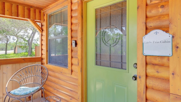 A wooden cabin with a green door, a wicker chair, and a sign reading "Little Frio Cabin." - Cozy Couple's Cabin Retreat in Concan! (Concan)