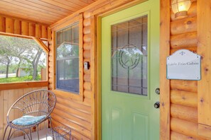 A wooden cabin with a green door, a wicker chair, and a sign reading "Little Frio Cabin." - Cozy Couple's Cabin Retreat in Concan! (Concan)