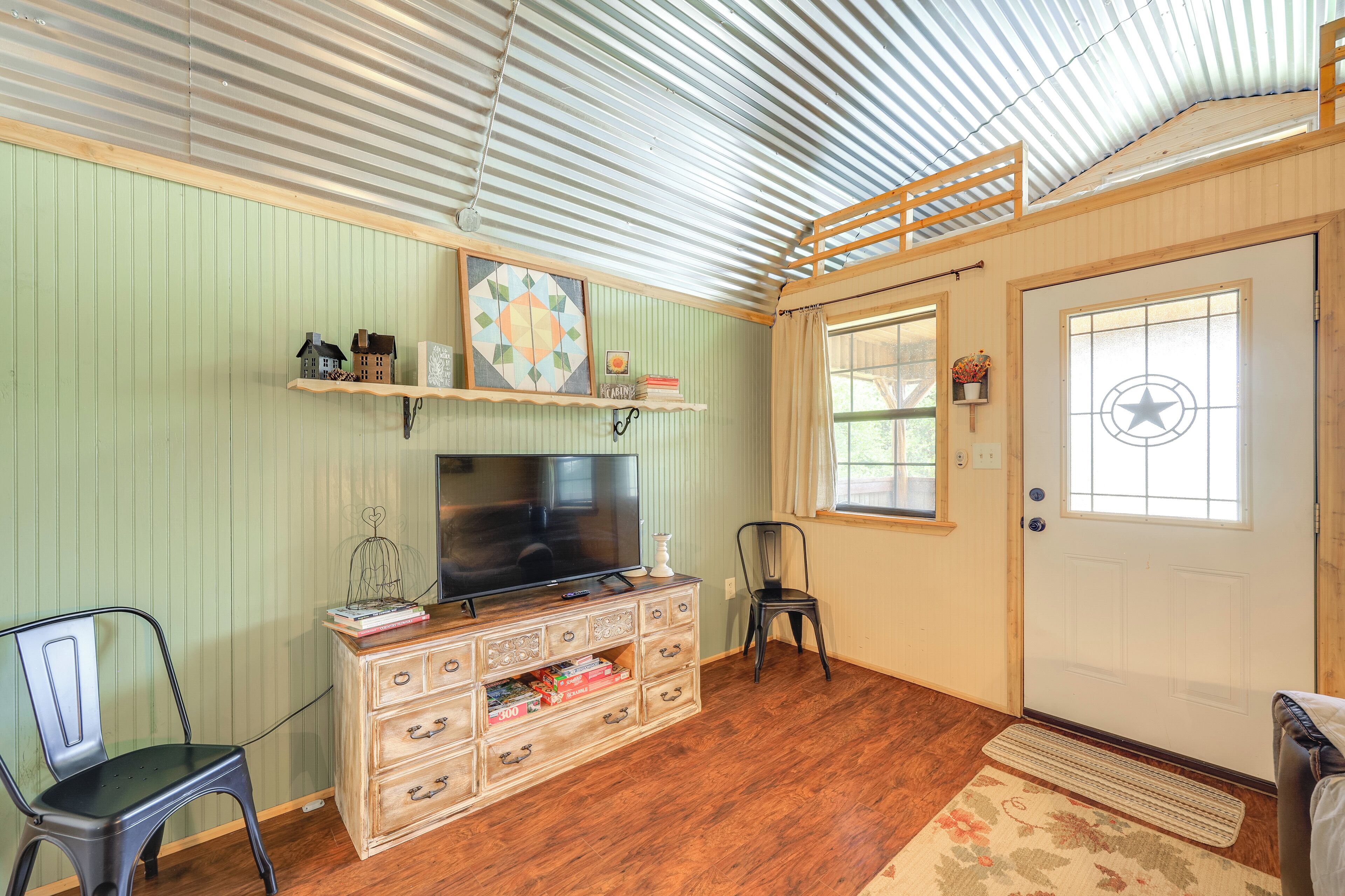 A room with a television on a wooden dresser, a chair, a shelf with decorative items, and a door with a star symbol.
