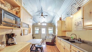 A kitchen with wooden cabinets, a coffee maker, a microwave, and a dining area with a table and chairs. - Cozy Couple's Cabin Retreat in Concan! (Concan)