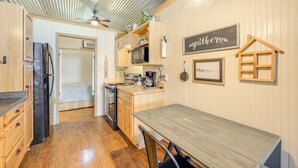 A compact kitchen with wooden cabinets, a refrigerator, a microwave, and a coffee maker. There is a dining table with chairs and a hanging light fixture. - Cozy Couple's Cabin Retreat in Concan! (Concan)