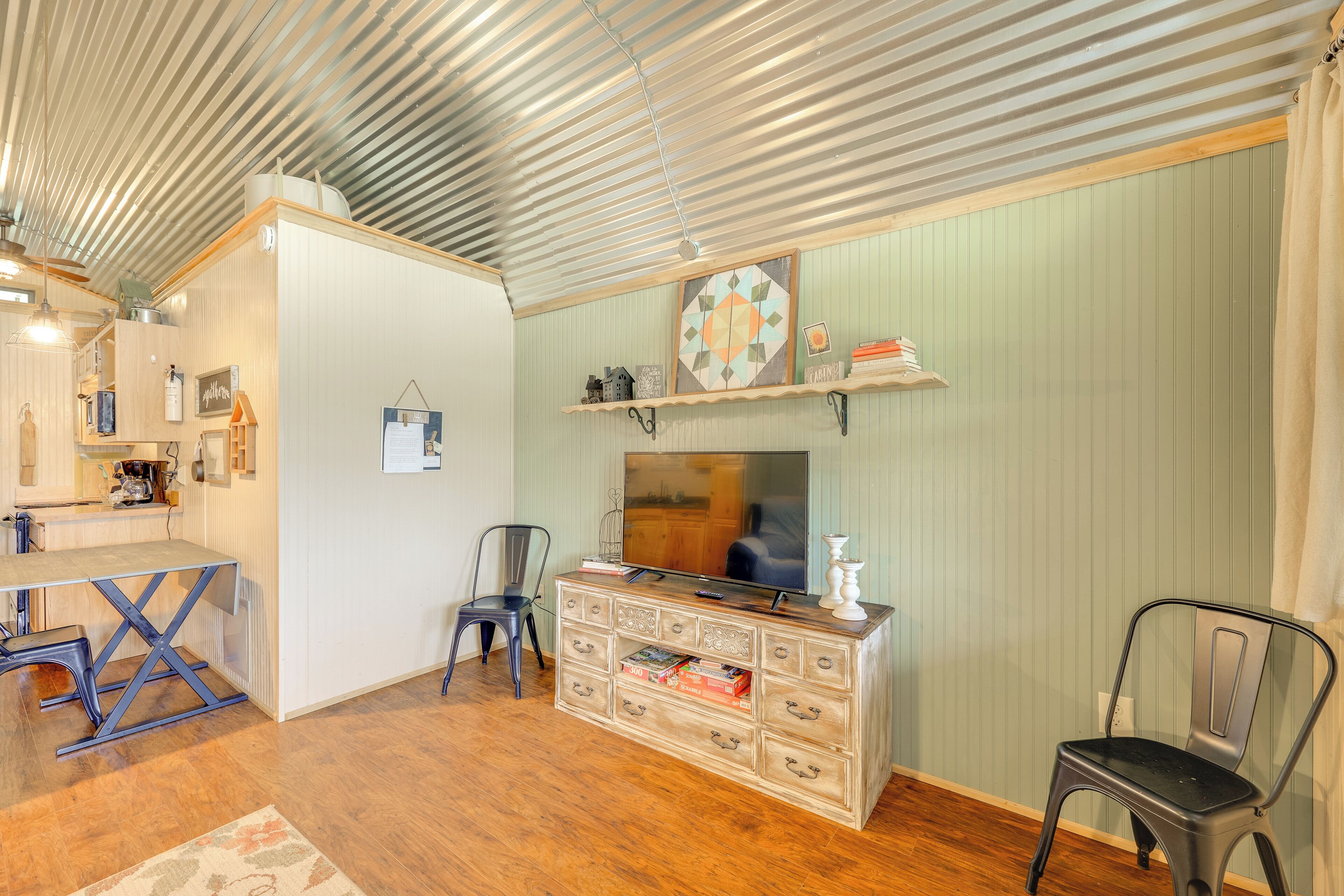 A room with a wooden floor, a TV on a dresser, a chair, and a shelf with decorative items.