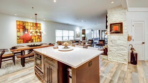 A spacious kitchen with a large island, wooden cabinetry, and a dining area with a bench. - Modern Condo + Golf Course View, Near Hiking! (Clayton)