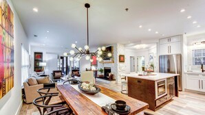 A modern kitchen with a wooden dining table, white cabinets, and a central island. - Modern Condo + Golf Course View, Near Hiking! (Clayton)