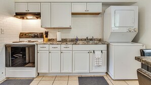 Cocina compacta con gabinetes blancos, estufa, lavamanos y lavadora.