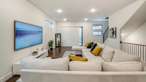 A modern living room with a sectional sofa, a flat-screen TV, and a staircase leading to an upper level. - 10 Mi to Dtwn Dallas: Sleek Retreat w/ Balcony (Dallas)