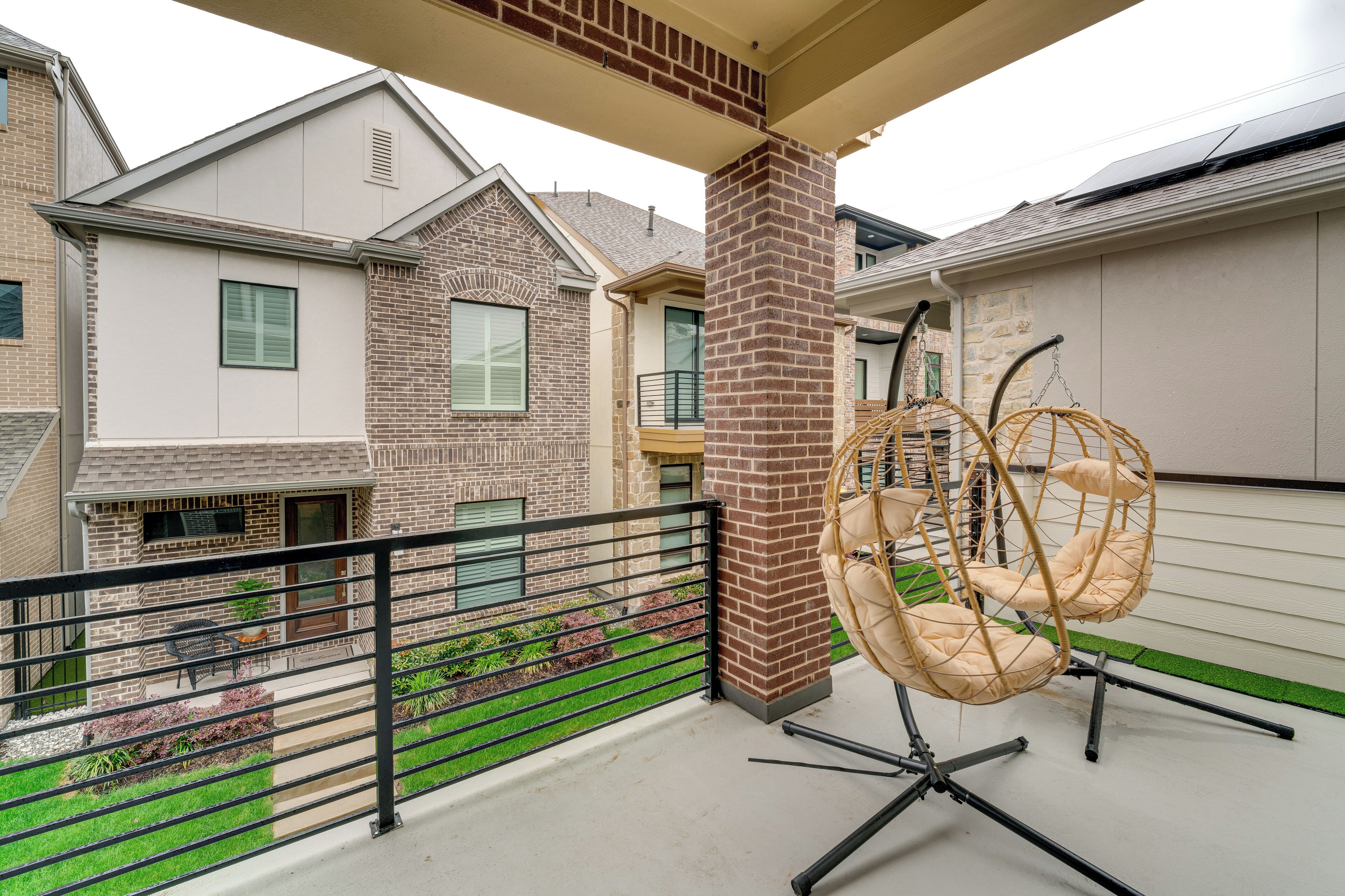 A balcony with hanging chairs, a brick pillar, and a view of neighboring houses.