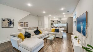 A modern living room with a sectional sofa, a glass coffee table, and a kitchen in the background. - 10 Mi to Dtwn Dallas: Sleek Retreat w/ Balcony (Dallas)