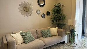 Una sala de estar con un sofá color beige, cojines estampados, un espejo y una planta en maceta.