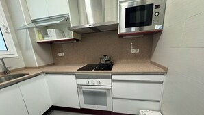 Una cocina compacta con armarios blancos, un microondas de acero inoxidable, una estufa a gas y un horno empotrado.