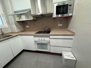 Una cocina compacta con armarios blancos, un microondas de acero inoxidable, una estufa a gas y un horno empotrado.