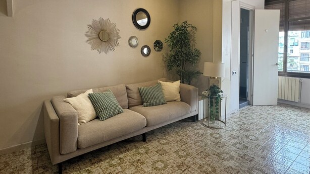 Una sala de estar con un sofá color crema, espejos decorativos y una planta en maceta.