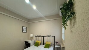Un dormitorio pequeño y ordenado con cama, mesita de noche, lámpara y una pequeña mesa redonda con un florero.