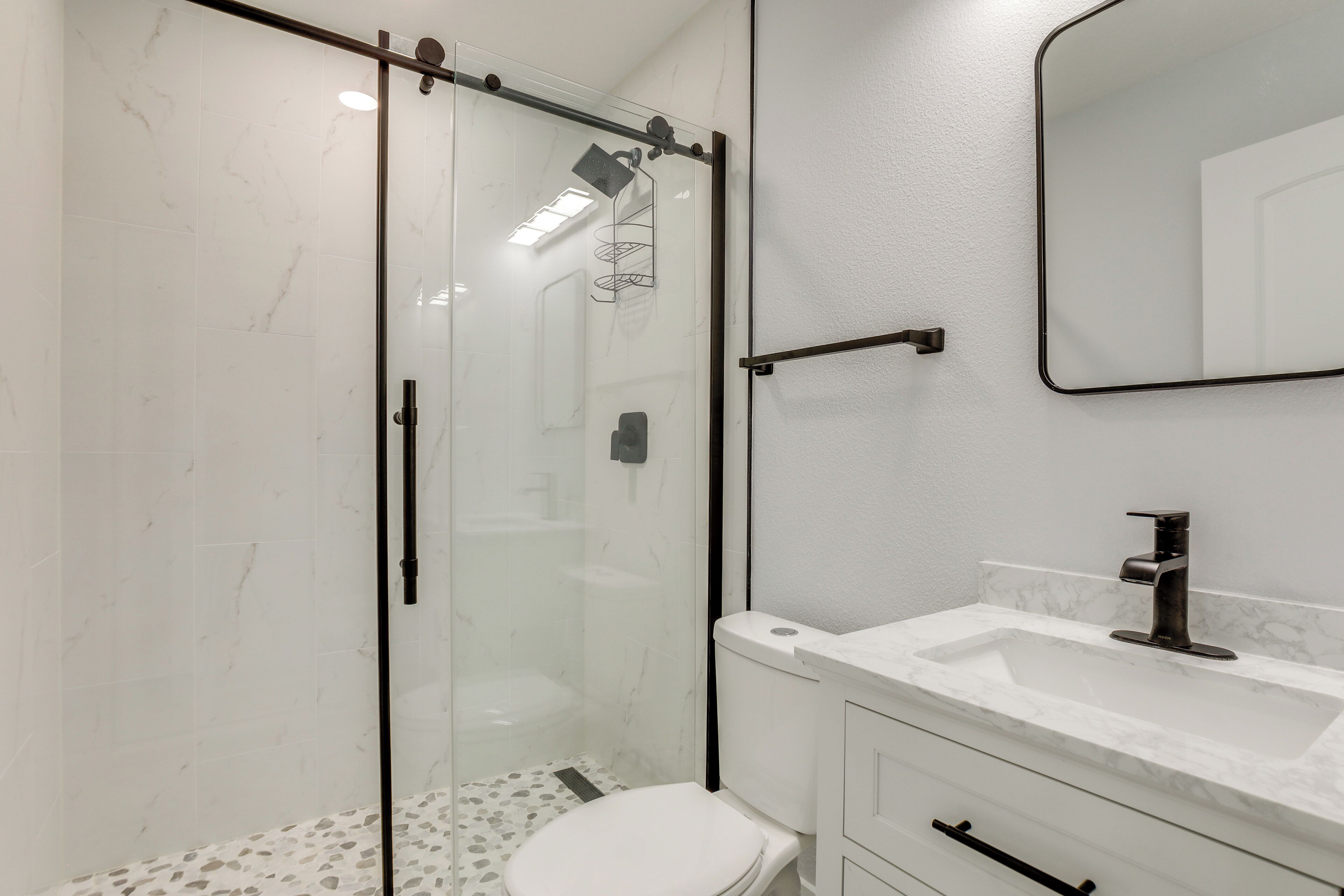 A modern bathroom with a glass shower enclosure, a white marble sink, and a large mirror.