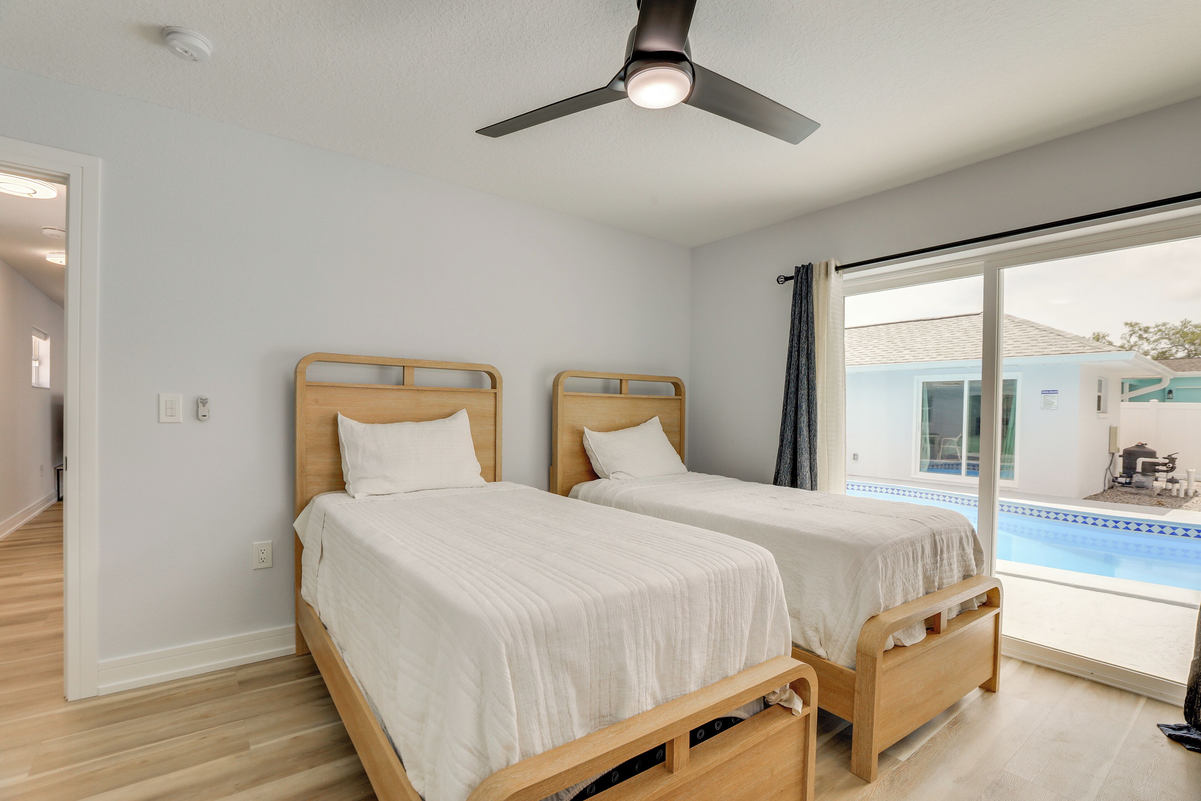 Une chambre avec deux lits en bois, un ventilateur de plafond et une vue sur une piscine.