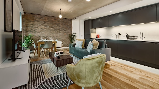 A modern living room with a dining area, a grey sofa, a green armchair, and a kitchen with dark cabinets and a white countertop. - Smart Northern Quarter Retreat (Manchester)