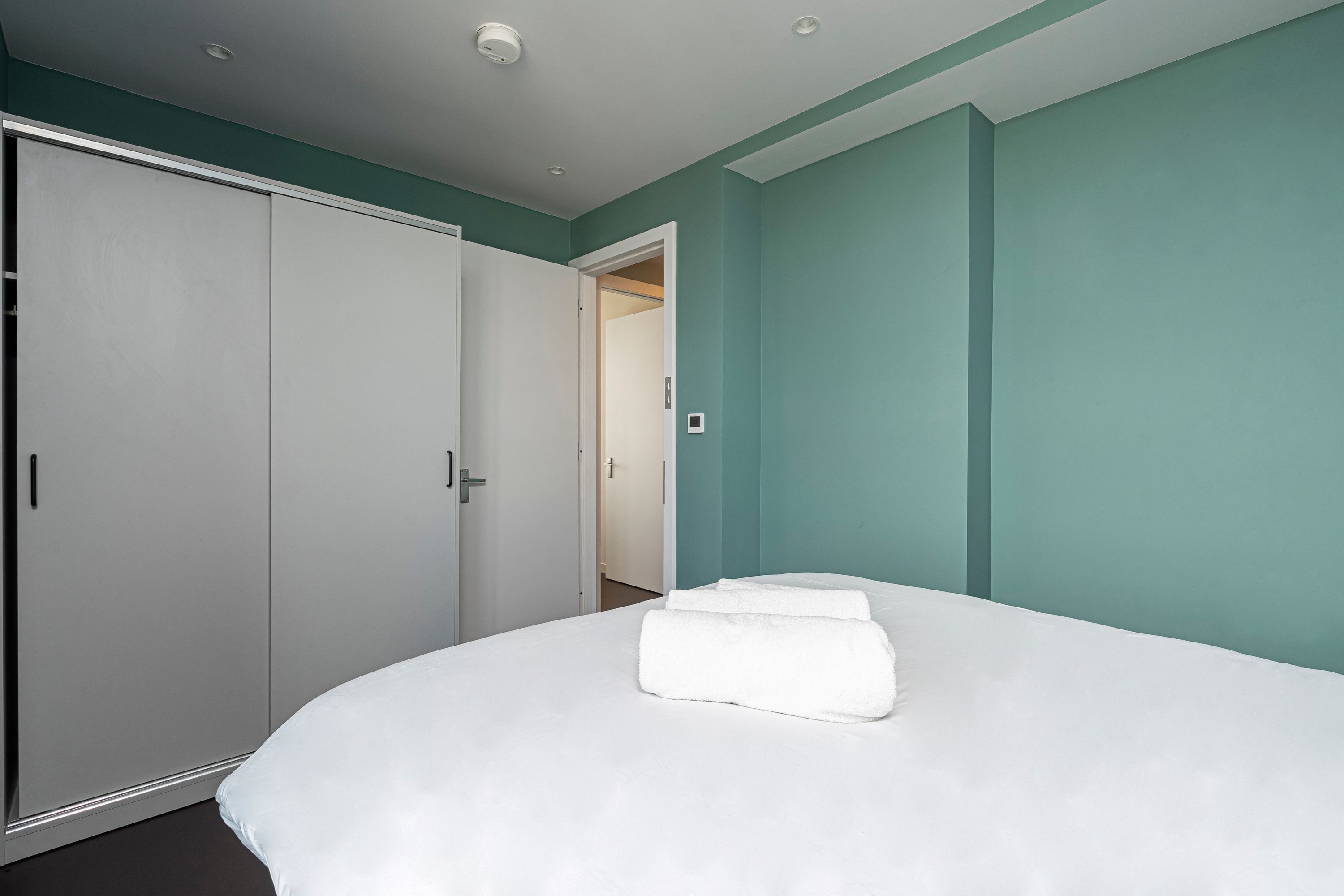 A bedroom with a large bed, a wardrobe, and teal walls.