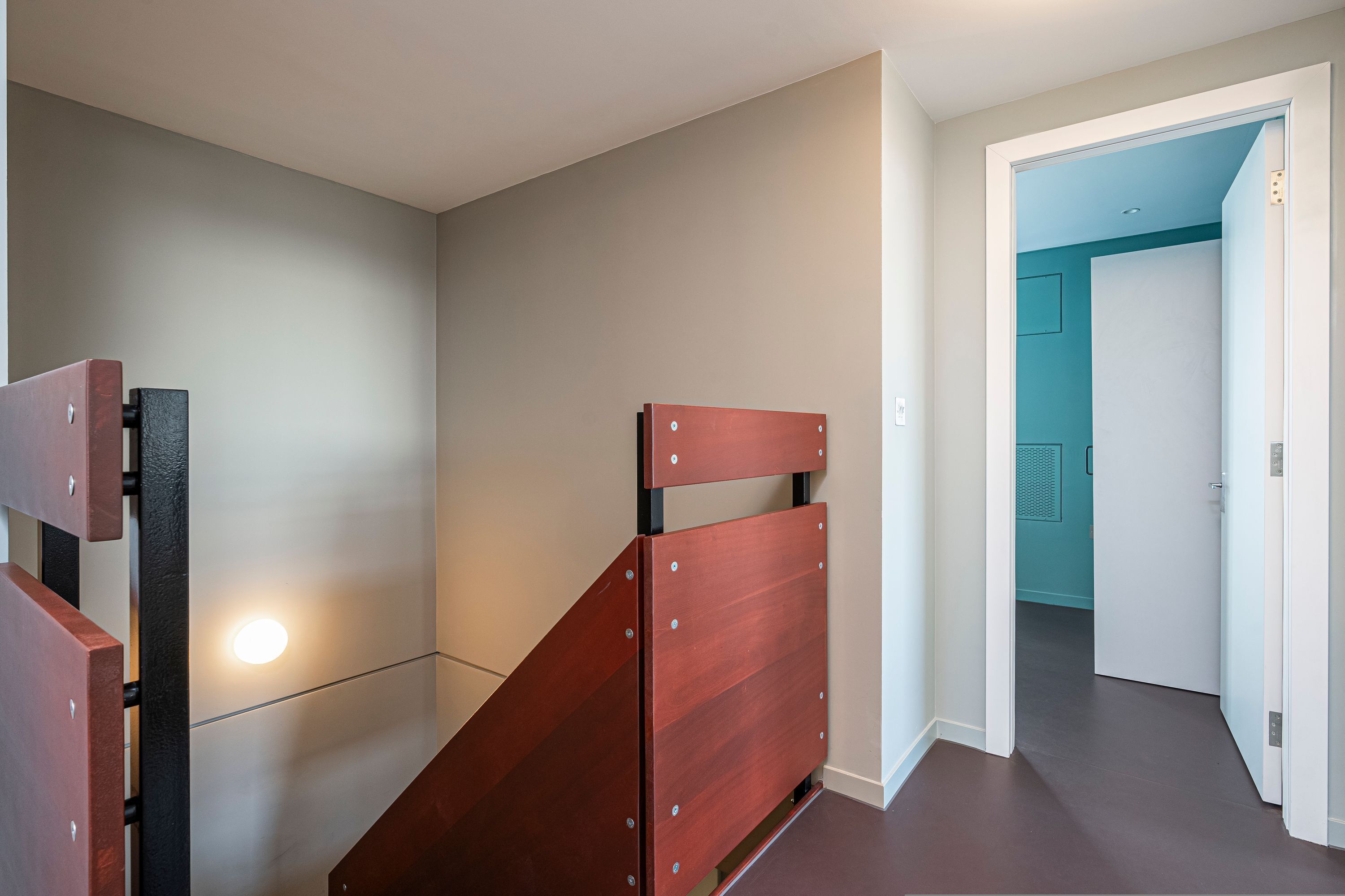 A room with a wooden bed frame, a light fixture on the wall, and a teal-colored door in the background.