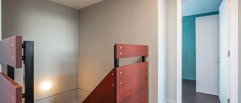A room with a wooden bed frame, a light fixture on the wall, and a teal-colored door in the background.