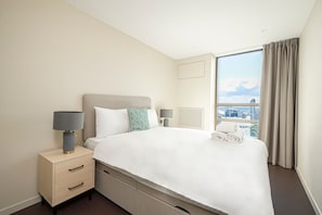 A hotel room with a bed, a nightstand with a lamp, a window with curtains, and a city view.