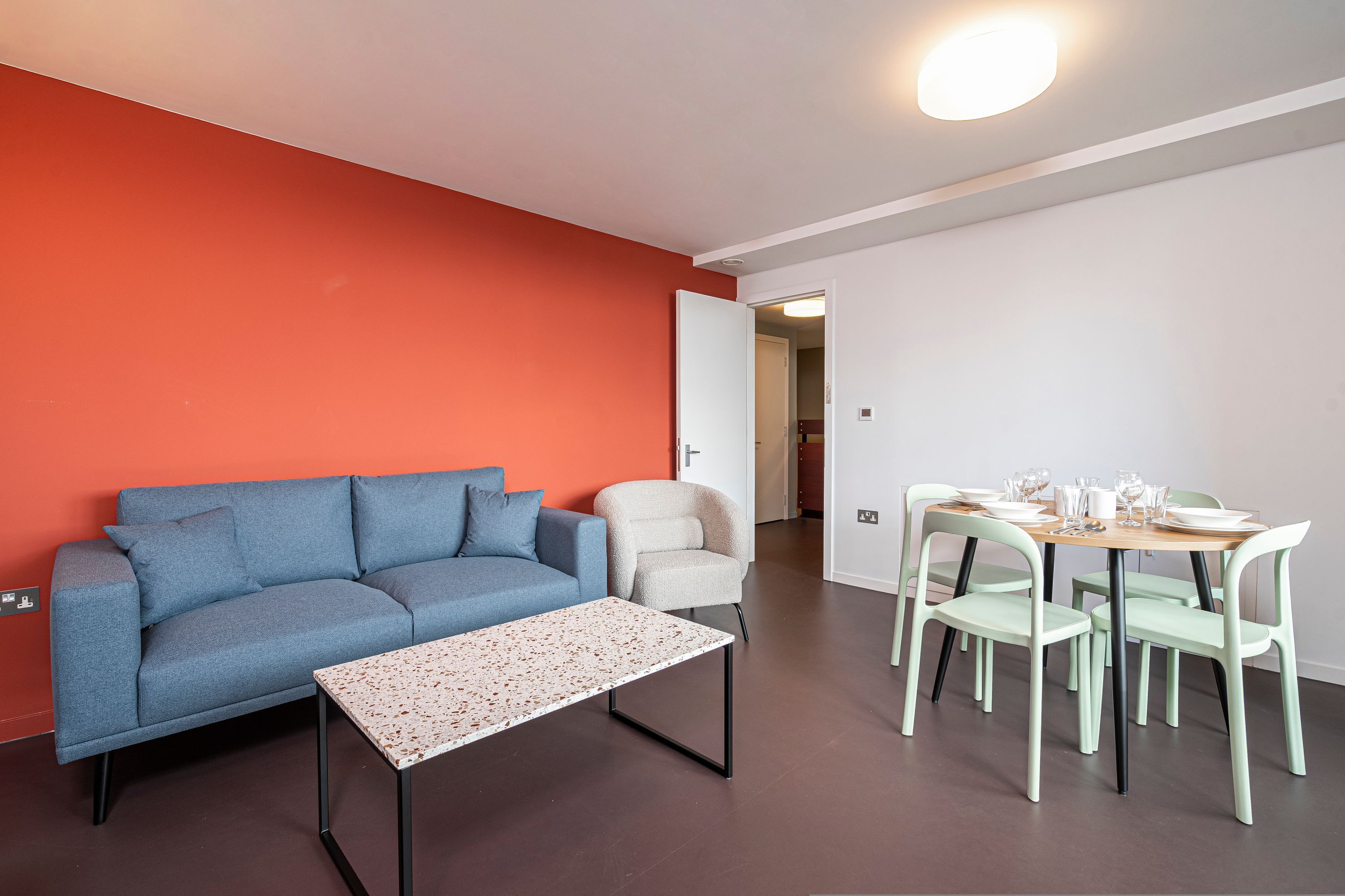 Una sala de estar moderna con un sofá azul, una mesita y una zona de comedor con una mesa de madera y sillas verdes.