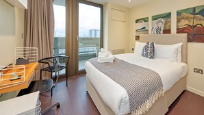 Une chambre d’hôtel équipée d’un lit, d’un bureau, d’une chaise et d’un balcon donnant sur des immeubles.