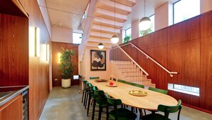 Un espace repas moderne avec une longue table en bois, des chaises vertes et un escalier doté d’une rampe en bois.