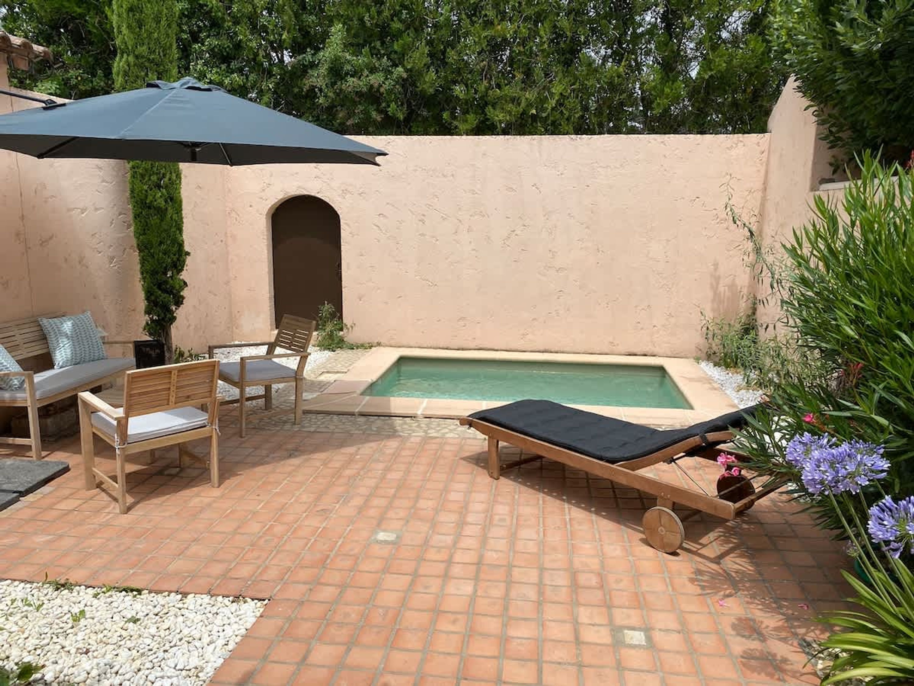 A patio with a pool, outdoor furniture, and a large umbrella.
