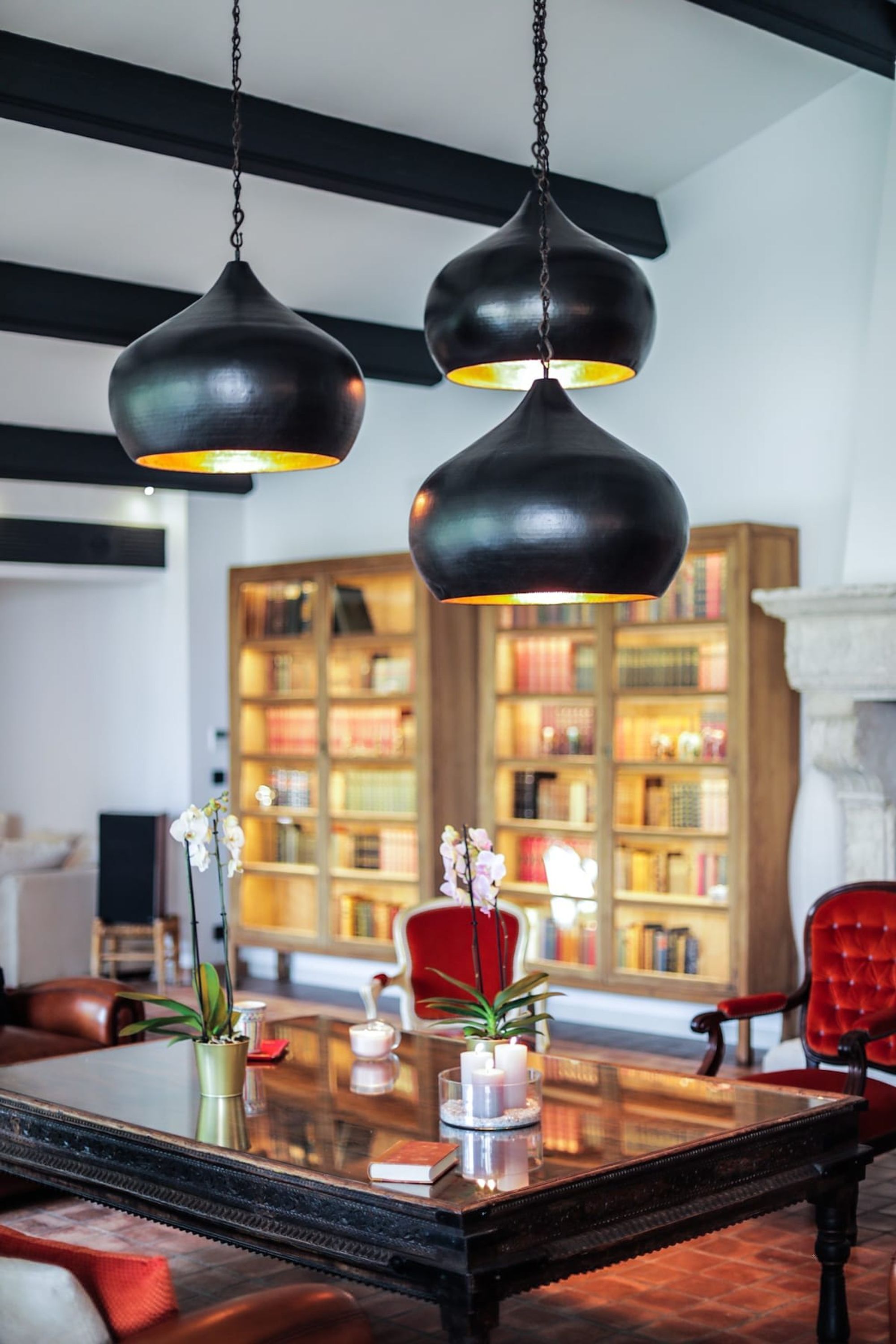 A dining area with a glass table, red chairs, and black hanging pendant lights.