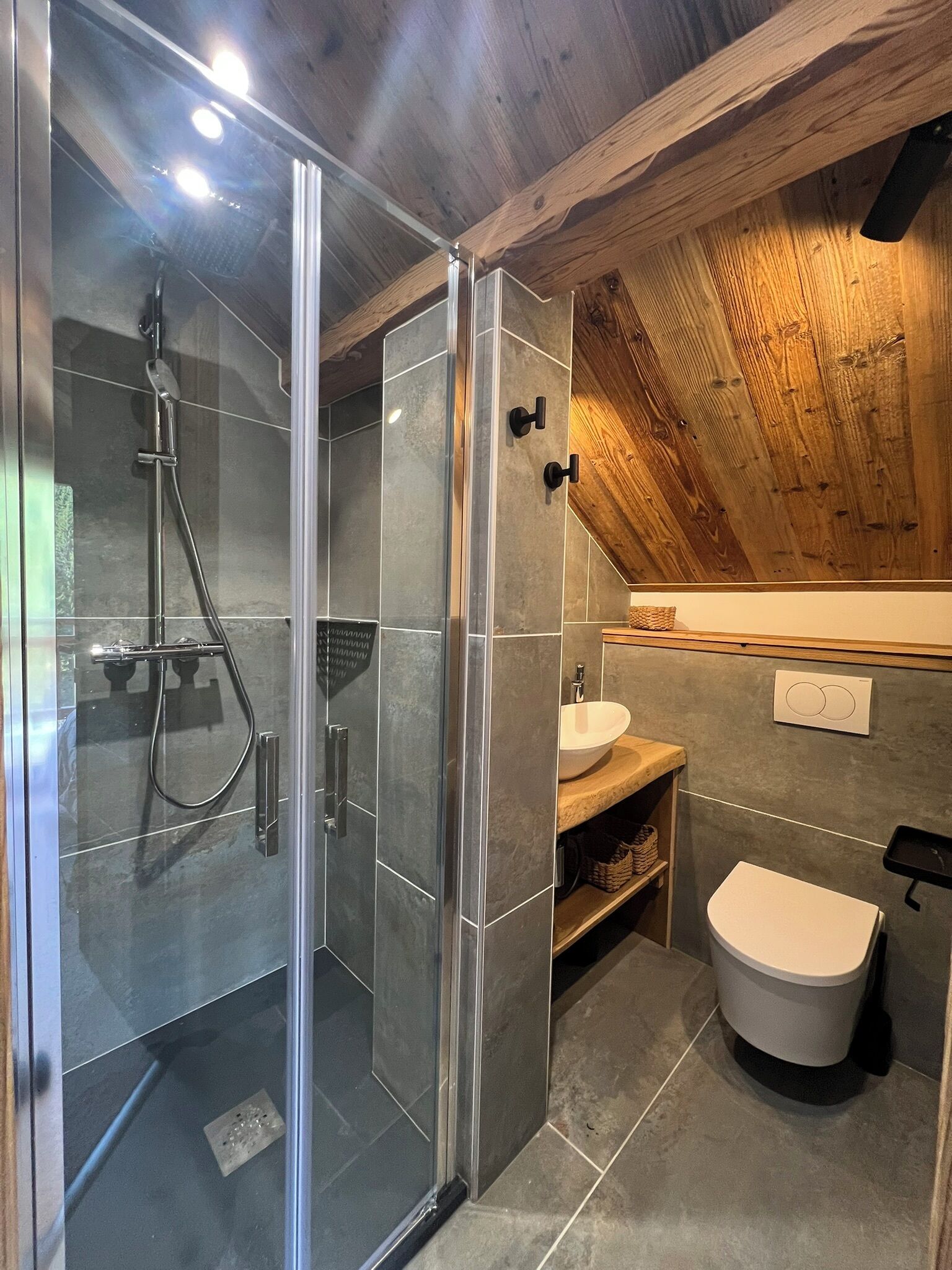 Un baño moderno con cabina de ducha de vidrio, techo de madera y un inodoro blanco.