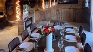 Un espace repas avec une longue table dressée pour six personnes, entouré de murs en bois et d’un plafond en bois avec des poutres apparentes.