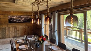 A wooden interior with a dining table set for four, surrounded by chairs, and a hanging light fixture with a rustic design. - Le Refuge du Grand-père spa/sauna (Taninges)