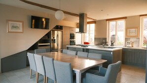 A modern kitchen with a dining area, built-in appliances, and large windows. - Charming stone house 13 p, private garden & fireplace near Baie de Somme (Beauchamps)