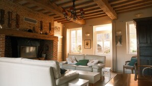 A cozy living room with a fireplace, a sofa, and a dining table. - Charming stone house 13 p, private garden & fireplace near Baie de Somme (Beauchamps)
