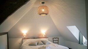 A bedroom with a sloped ceiling, a bed with pillows, two bedside lamps, and a hanging light fixture. - Charming stone house 13 p, private garden & fireplace near Baie de Somme (Beauchamps)