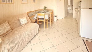 A cozy room with a wooden ceiling, a dining table with chairs, a sofa, and a kitchen area with a refrigerator. - Comfortable waterfront apartment with breathtaking views, nature break (Anthy-sur-Léman)