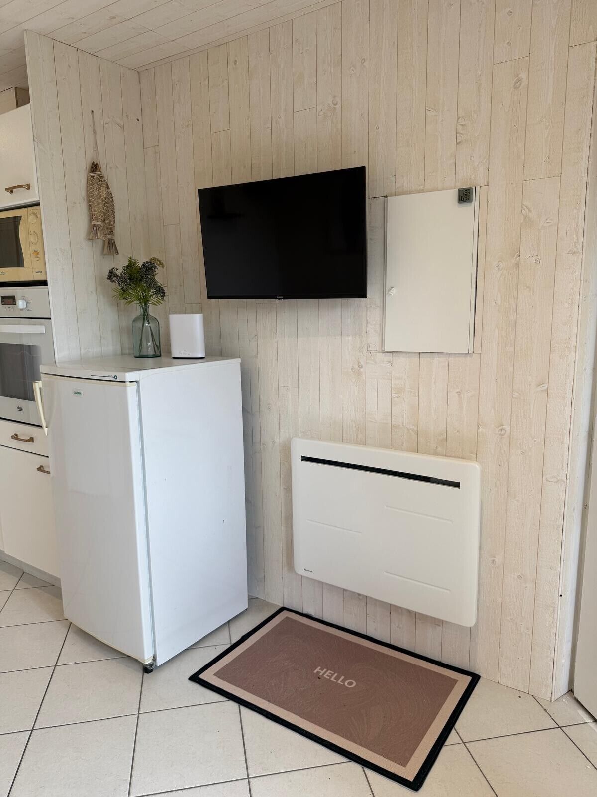 Eine kompakte Küche mit integriertem Mikrowellenherd, einem weißen Kühlschrank, einem Flachbildfernseher und einem weißen Schrank.