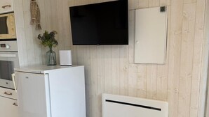 A compact kitchen with a built-in microwave, a white refrigerator, a flat-screen TV, and a white cabinet. - Comfortable waterfront apartment with breathtaking views, nature break (Anthy-sur-Léman)