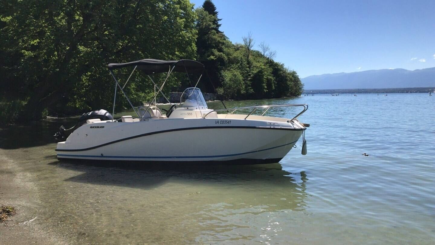Ein Boot liegt an einem See mit bewaldetem Ufer und Bergen im Hintergrund.