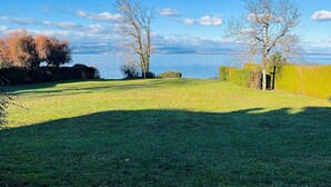 A grassy lawn with a view of a body of water and distant mountains. - Comfortable waterfront apartment with breathtaking views, nature break (Anthy-sur-Léman)