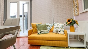 Una sala de estar acogedora con un sofá amarillo, una mesita blanca y un jarrón con girasoles.