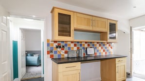 Una cocina compacta con armarios de madera, salpicadero de azulejos y encimera negra.