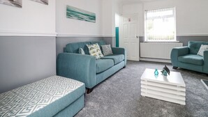 Un salón moderno con sofás azul verdoso, cojines estampados y una mesa de centro blanca.