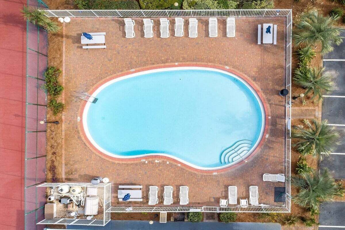 Eine Vogelperspektive auf einen Swimmingpool, umgeben von Liegestühlen und einem Gebäude mit Dach.