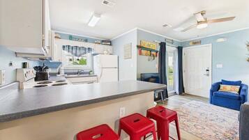 Une cuisine compacte avec un îlot central, un coin repas avec une chaise bleue et un tabouret rouge.
