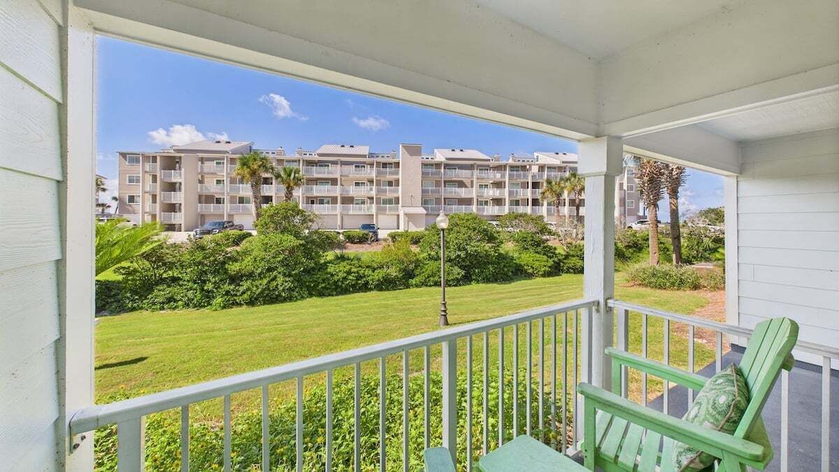 A balcony with a view of a multi-story building, a lawn, and a green chair.