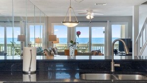 A modern kitchen with a large window overlooking the sea, a ceiling fan, and a dining area with a view.