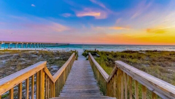 A wooden boardwalk leading to a beach with a pier in the background.